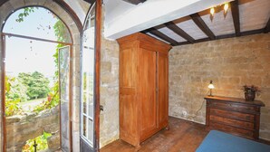 Quarto rústico com guarda-roupa de madeira, penteadeira e uma grande janela em arco.