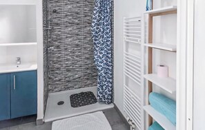 Une salle de bain avec une baignoire, une douche et des toilettes. On y trouve une étagère avec une serviette et un rouleau de papier toilette.