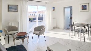 A spacious living area with a large sliding glass door leading to a balcony, a dining area with a table and chairs, and a small side table with a bowl. - Beautiful apartment in Dunkerque with WiFi (Dunkerque)