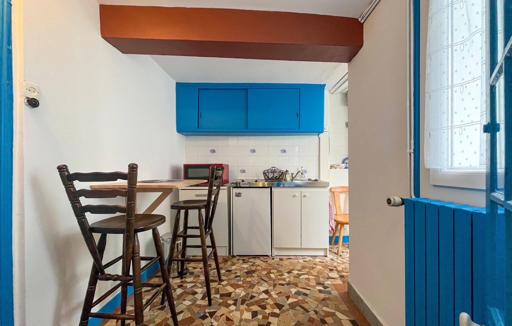 A small kitchen with blue cabinets, a tiled backsplash, and a patterned floor.