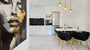 Een moderne keuken met witte kasten, een zwart aanrecht en gouden accenten. Er is een eethoek met een witte tafel en zwarte stoelen.