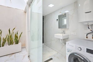 Un bany modern amb plat de dutxa de vidre, un lavabo blanc i rentadora integrada.