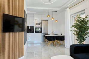 A modern kitchen with a flat-screen TV, a dining area with a table and chairs, and a large potted plant.