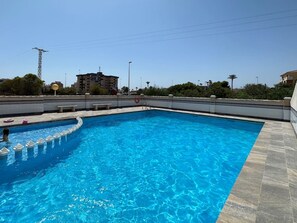 A rectangular swimming pool with a tiled edge, surrounded by a low wall and a flat roof.