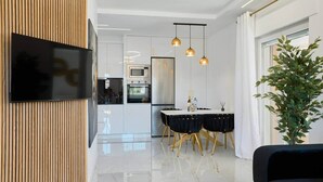 Een moderne keuken met witte kastjes, een ingebouwde oven en een eethoek met een witte tafel en zwarte stoelen.