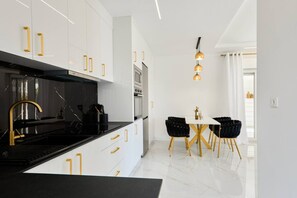 A modern kitchen with white cabinets, gold handles, a black countertop, and a dining area with a white table and black chairs.