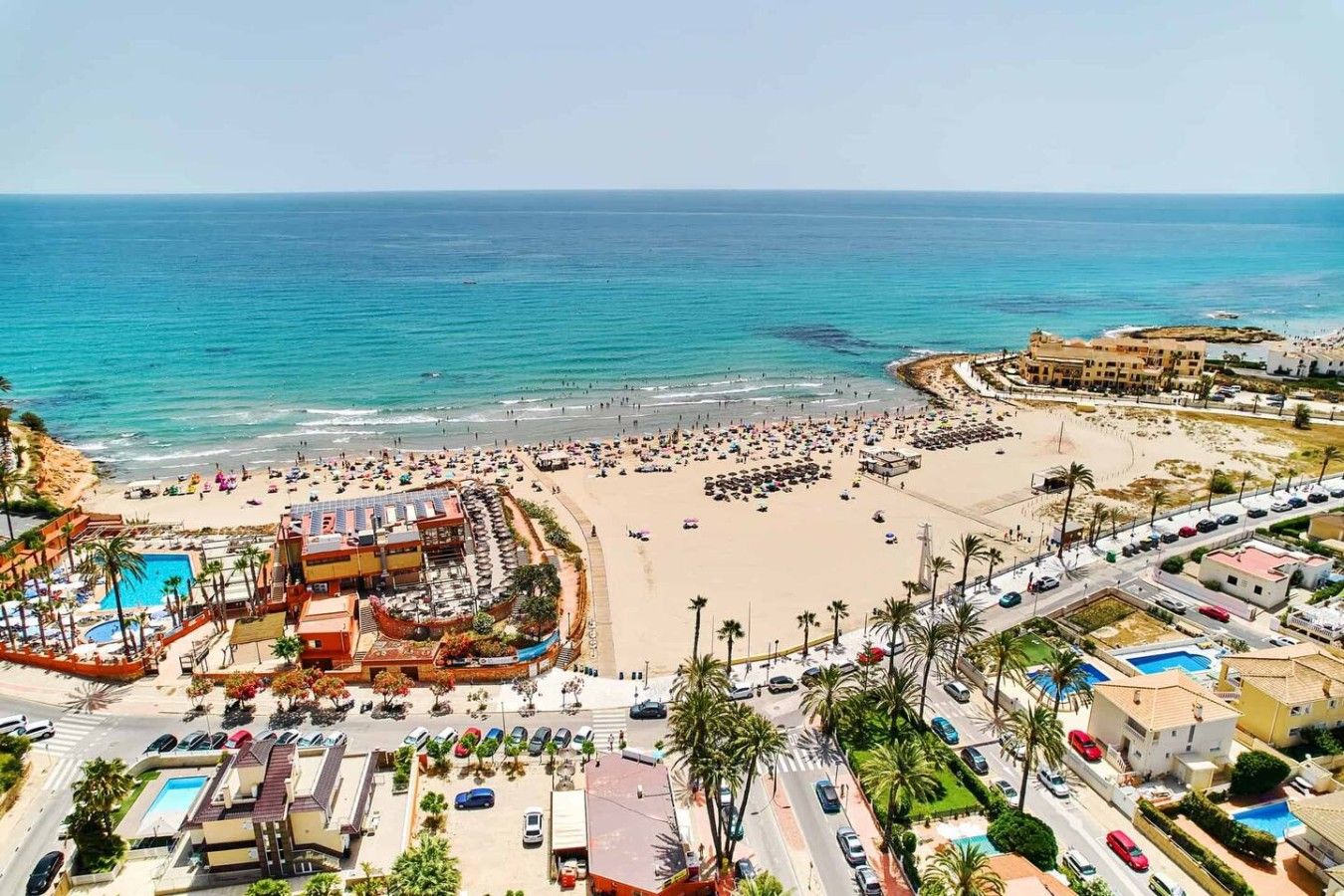 A coastal resort with a beach, swimming pool, and parking area.