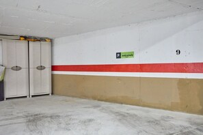A parking garage with a white wall, a red stripe, and a beige section. There is a sign for 'Holiday Rentals' and a parking symbol. - Conquistador C (El Campello)