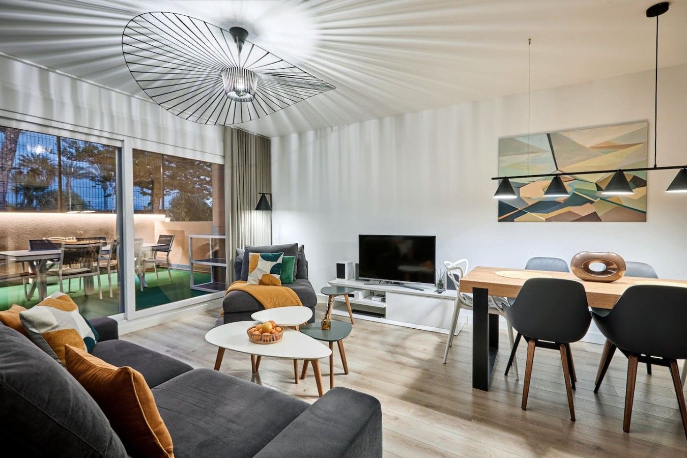 Un salon moderne doté d’un téléviseur à écran plat, d’un coin repas avec une table et des chaises en bois, et d’une grande fenêtre offrant une vue sur l’extérieur.