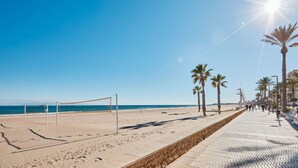 A beach with a volleyball net, palm trees, and a paved walkway. - Conquistador C (El Campello)