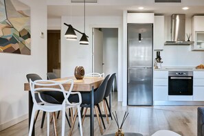 A modern kitchen with a stainless steel refrigerator, a built-in oven, and a dining area with a wooden table and chairs. - Conquistador C (El Campello)
