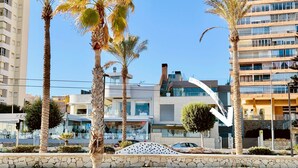 Un bâtiment moderne doté d’une façade en verre incurvée, de palmiers et d’un mur de pierre au premier plan.