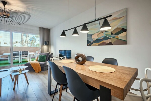 A modern dining area with a wooden table, black chairs, and pendant lighting.