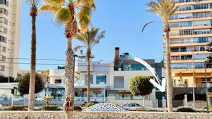 A beachfront property with modern architecture, palm trees, and a clear sky. - Conquistador C (El Campello)