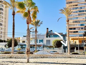 A beachfront property with modern architecture, palm trees, and a clear sky.