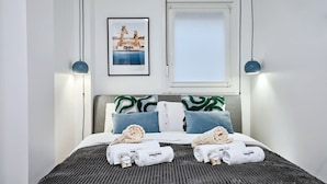 A neatly made bed with a striped bedspread, two pillows with green and white patterns, and two rolled towels with a logo. - Conquistador C (El Campello)