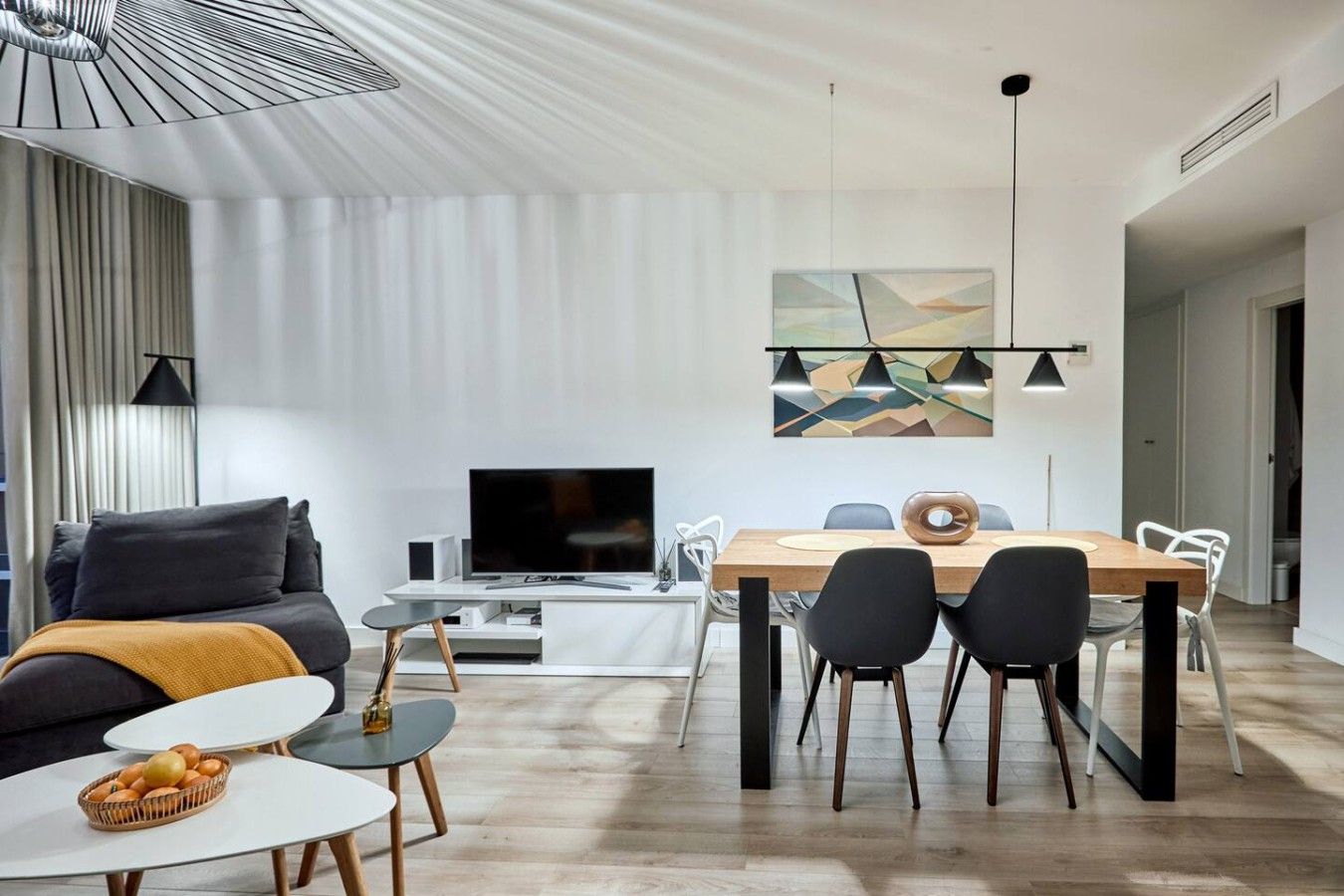 A modern living room with a flat-screen TV, a dining area with a wooden table and chairs, and a large abstract painting on the wall.