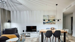 A modern living room with a flat-screen TV, a dining area with a wooden table and chairs, and a large abstract painting on the wall. - Conquistador C (El Campello)