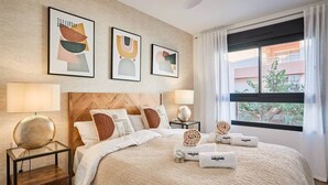 A hotel room with a large bed, two bedside tables with lamps, a wooden headboard, and three abstract wall art pieces.