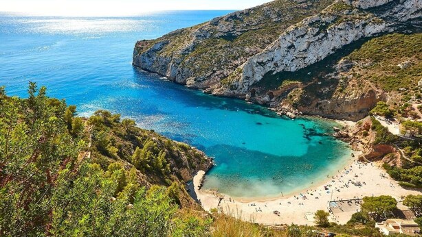 A coastal landscape with a beach, rocky cliffs, and clear blue waters. - Taylor Apartment (Xàbia)