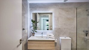 A modern bathroom with a wooden vanity, a potted plant, a towel, and a shower.
