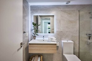 Un baño moderno con un tocador de madera, una planta en maceta, una toalla y una ducha.