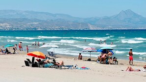 Uma praia com pessoas se banhando, nadando e caminhando pela orla.