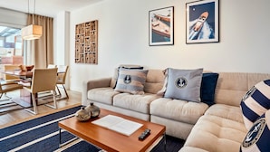 Un salon moderne avec un canapé beige, une table basse en bois et un coin repas comprenant une table et des chaises en bois.