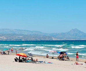 A beach with people sunbathing, swimming, and walking along the shore.