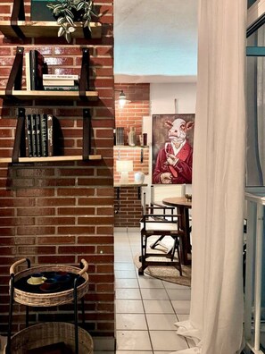 Een gezellig interieur met een bakstenen muur, boekenkasten, een rieten stoel, een eettafel en een schilderij van een varken.