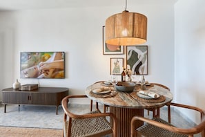 A dining area with a round table, wicker chairs, and a hanging light fixture.