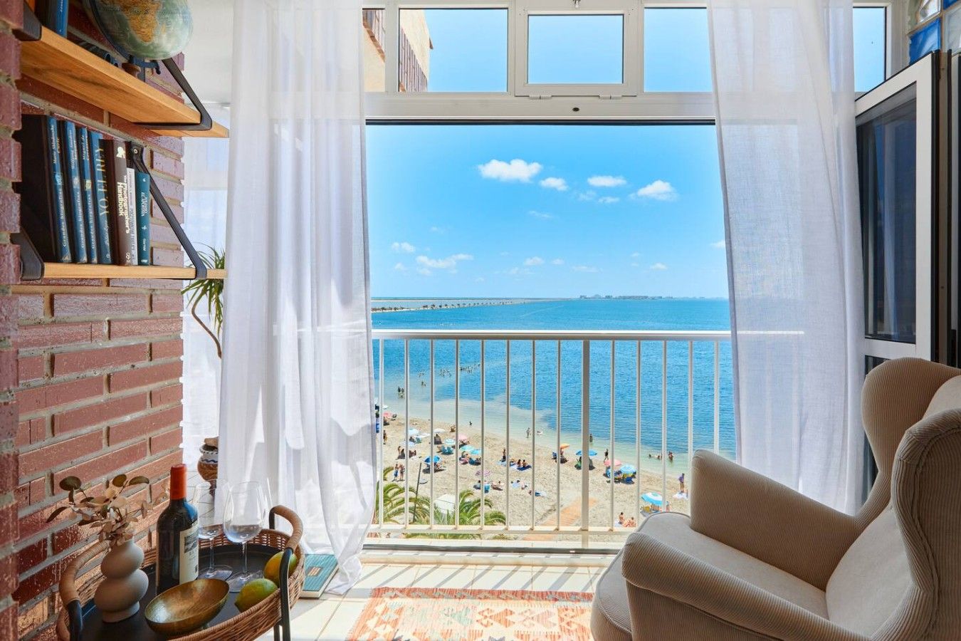 A balcony with a view of a beach, a brick wall, and a bookshelf.