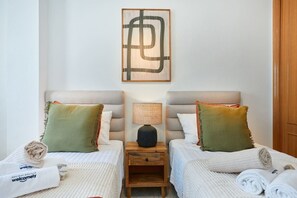 A hotel room with two beds, a nightstand with a lamp, and a wall-mounted artwork.