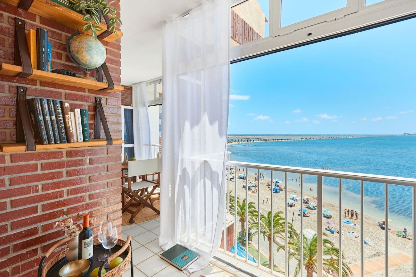 Un balcón con vista a una playa y un muro de ladrillo con estanterías.
