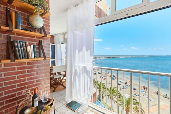 A balcony with a view of a beach and a brick wall with bookshelves.