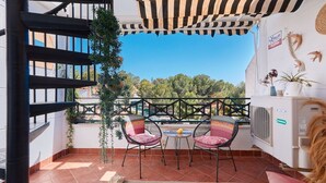 A balcony with a view, two wicker chairs, a small table, and a potted plant.
