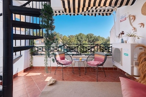 A balcony with a view, two wicker chairs, a small table, and a potted plant.