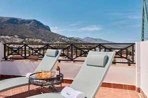 A terrace with two lounge chairs, a basket of oranges, and a bottle of wine.