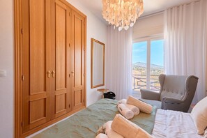Ein Schlafzimmer mit großem Kleiderschrank, einem Bett mit aufgerollten Handtüchern, einem Sessel und Blick ins Freie.