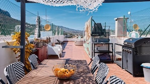 An outdoor patio with a table, chairs, a grill, and a view of the mountains.