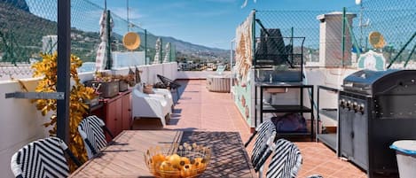 An outdoor patio with a table, chairs, a grill, and a view of the mountains.