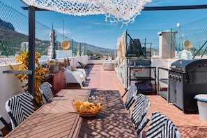 An outdoor patio with a table, chairs, a grill, and a view of the mountains.