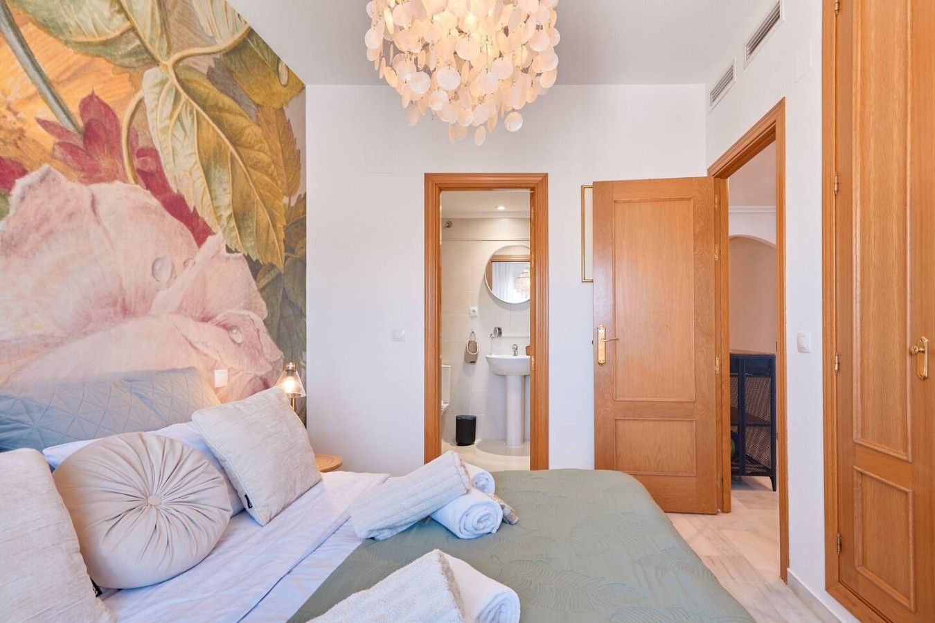 Ein Hotelzimmer mit einem Bett, einem großen Blumenwandteppich, einer Holztür und einem sichtbaren Badezimmer durch eine offene Tür.