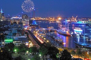 Stadsgezicht aan het water met een brug, boten en vuurwerk in de lucht.