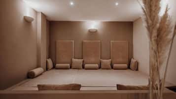 Quarto com cama alongada e discreta, luminária fixada na parede e uma planta alta e esguia em primeiro plano.