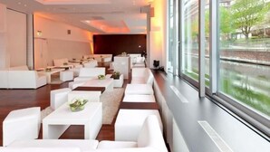 A modern hotel lobby with white sofas, tables, and a large window overlooking a river.