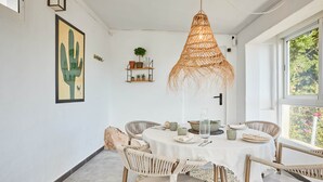Ein Essbereich mit einem runden Tisch, Korbstühlen, einer Hängeleuchte und Wandkunst mit Kaktusmotiven.