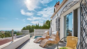 Eine Dachterrasse mit Korlounge-Möbeln, einem kleinen Tisch mit einer Flasche und einem Blumentopf.