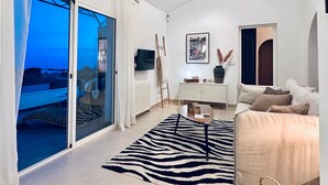 Ein modernes Wohnzimmer mit einer Couch, einem Couchtisch und einem Teppich mit ZEBRA-Muster. Ein Schiebeglastür führt zu einem Balkon mit Blick.