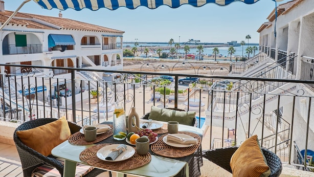 Un balcon avec une table préparée pour le petit-déjeuner, donnant sur une plage et des bâtiments.